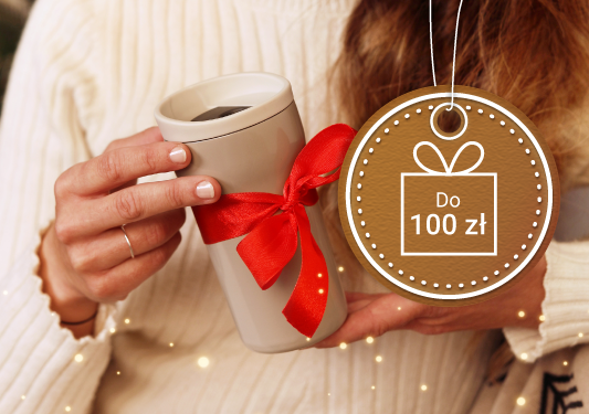 Grafika przedstawia kobietę w kremowym swetrze trzymającą kubek termiczny w beżowym kolorze przewiązany czerwoną wstążką. Obok zwisa okrągła etykieta przypominająca udekorowany lukrem pierniczek z napisem do 100 zł zamkniętym w ikonie prezentu.