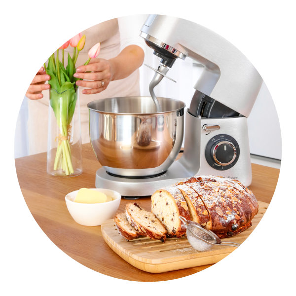 Metalowy robot kuchenny, obok którego na drewnianej desce leży chałka z rodzynkami.