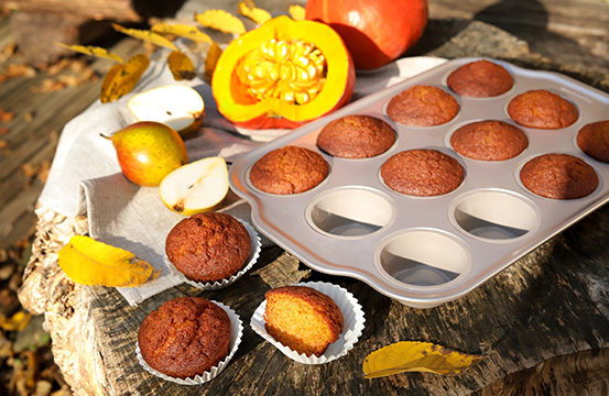 Na pniu drzewa leży silikonowa forma na 12 muffinów, która posiada metalowy brzeg. W formie znajduje się 9 dyniowo-gruszkowych muffinów, pozostałe trzy leżą w papierowych papilotkach poza formą. Wokół leżą pożółkłe liście, gruszki oraz dynie.