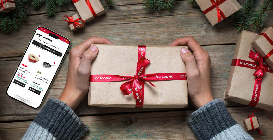 Grafika przedstawia dłonie osoby ubranej w niebieski sweter trzymające prostokątny prezent zapakowany w brązowy papier i obwiązany błyszczącą, czerwoną wstążką w białe napisy tescoma. Wokół leży więcej takich prezentów. Po lewej stronie leży smartfon, na którego ekranie wyświetlone są produkty na stronie Tescomy.