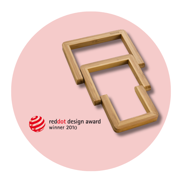 Grafika przedstawia drewnianą rozkładaną podstawkę ONLINE na jasnoróżowym tle. Obok podstawki widnieje informacja o tym, że produkt wygrał nagrodę reddot design award w 2010 roku.