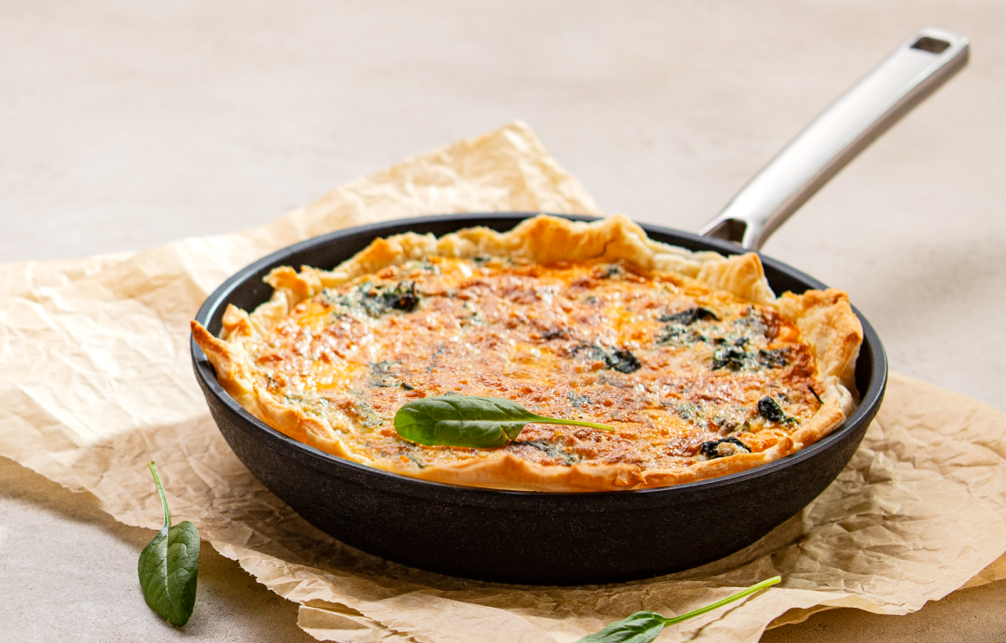Quiche z groszkiem i szpinakiem w czarnej patelni ze stalową rękojeścią.