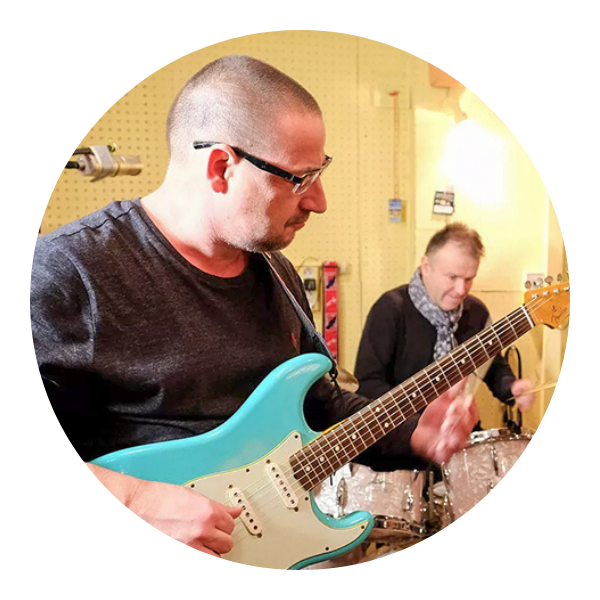 Opis: na pierwszym planie Jiří Vaculík gra na gitarze, w tle na perkusji gra Petr Chmela.