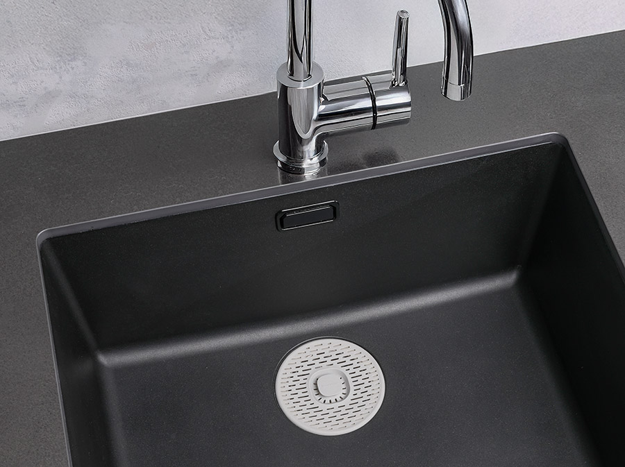 Szare silikonowe sitko w dużym czarnym zlewie.